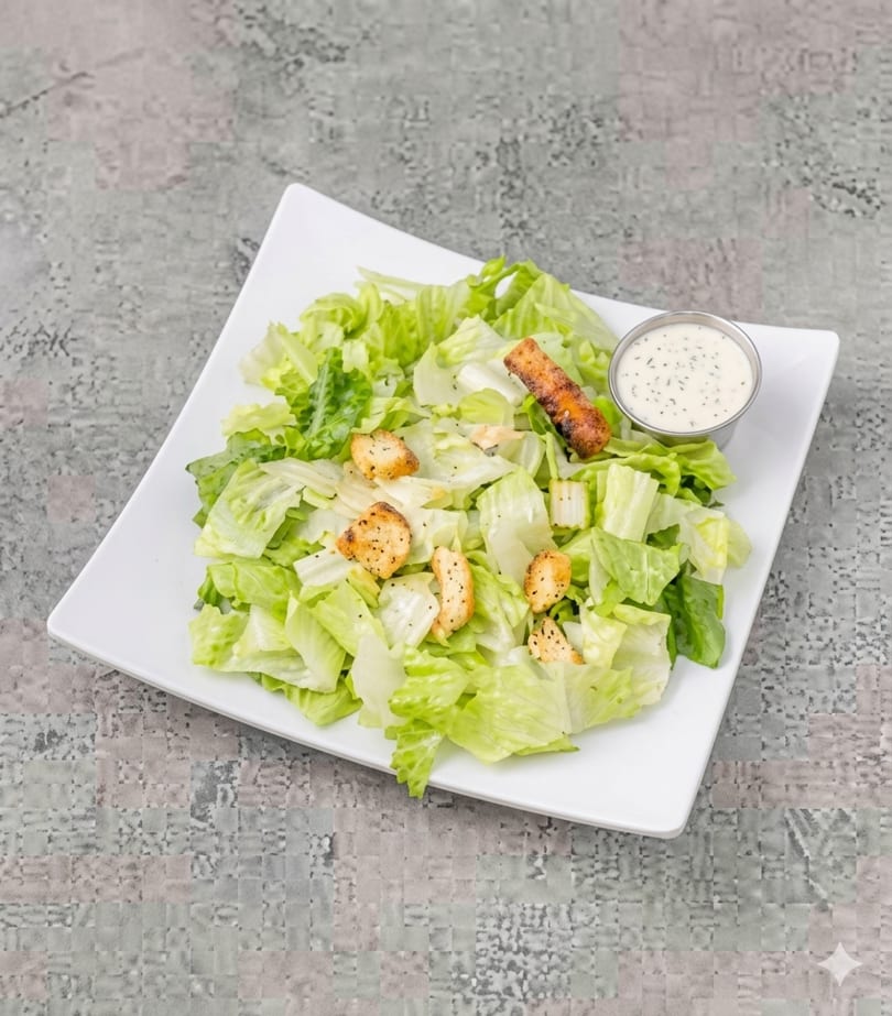 Fresh green salad with croutons and a side of creamy dressing on a white plate.