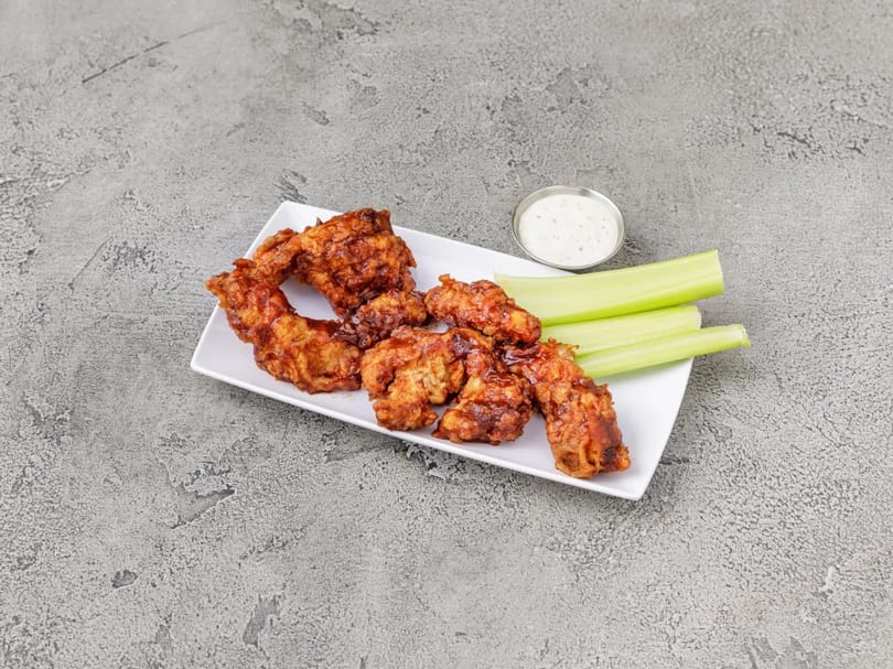 Crispy boneless wings with celery sticks and a side of ranch dressing on a white plate.